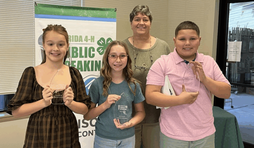 The Florida 4-H Public Speaking Contest winners proudly display their hardware while pictured with 4-H Director Beth Moore. Pictured in back is Moore. Pictured in front, from left to right, are: fourth-grade winner, Madilyn Fletcher; fifth-grade winner, Scarlett Brooks; and sixth-grade winner, Nicolas Gonzalez. See page 13 for more details on the speech contest. [Mickey Starling/Greene Publishing, Inc.]
